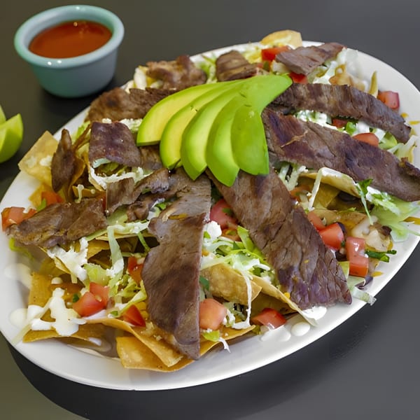 Galindos Kitchen's carne asada nachos with sliced avocado, sour cream, tomatoes, and lettuce.