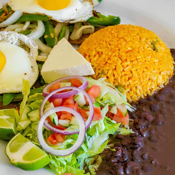 Mexican breakfast plate with fried eggs, rice, refried beans, salad, cheese, and lime wedges.