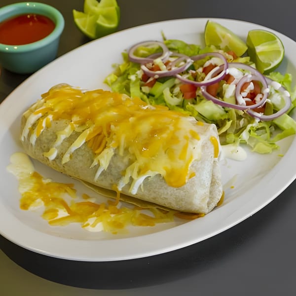 A Galindos Kitchen burrito topped with melted cheese and sour cream, served with a side salad and lime.