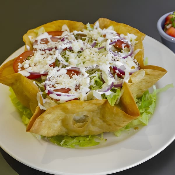 A Galindos Kitchen taco salad in a crispy tortilla bowl, topped with fresh vegetables, cheese, and sour cream.