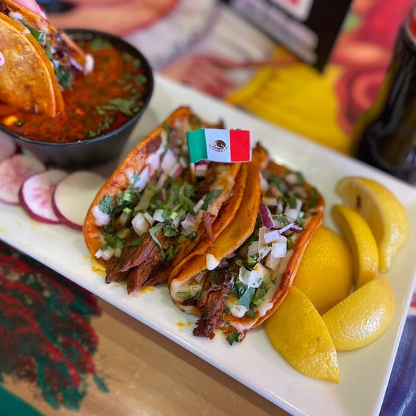 Three Galindos Kitchen birria tacos with consome, radishes, and lemons on a white plate.